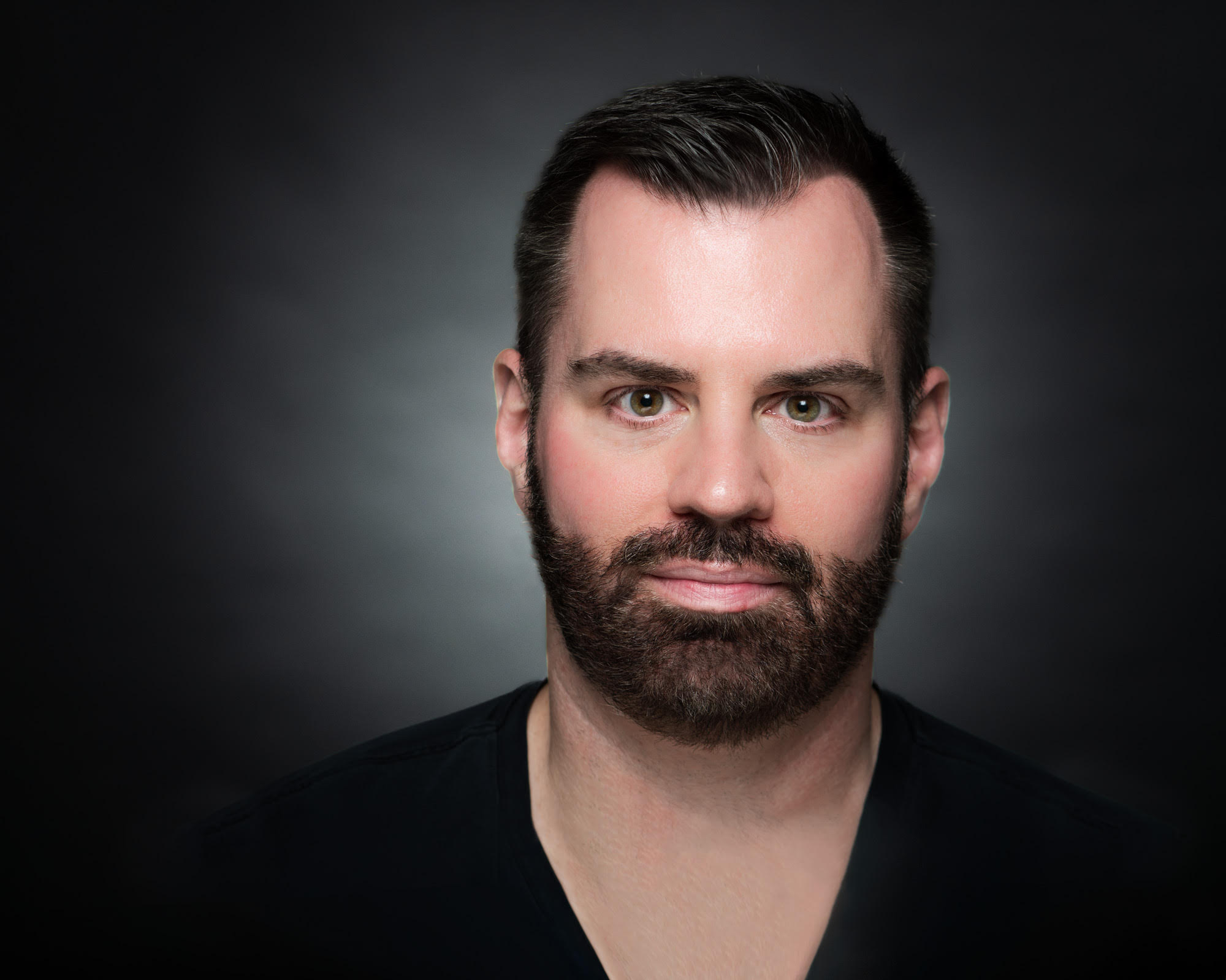A close up of a white man with short, dark black hair and a black beard 