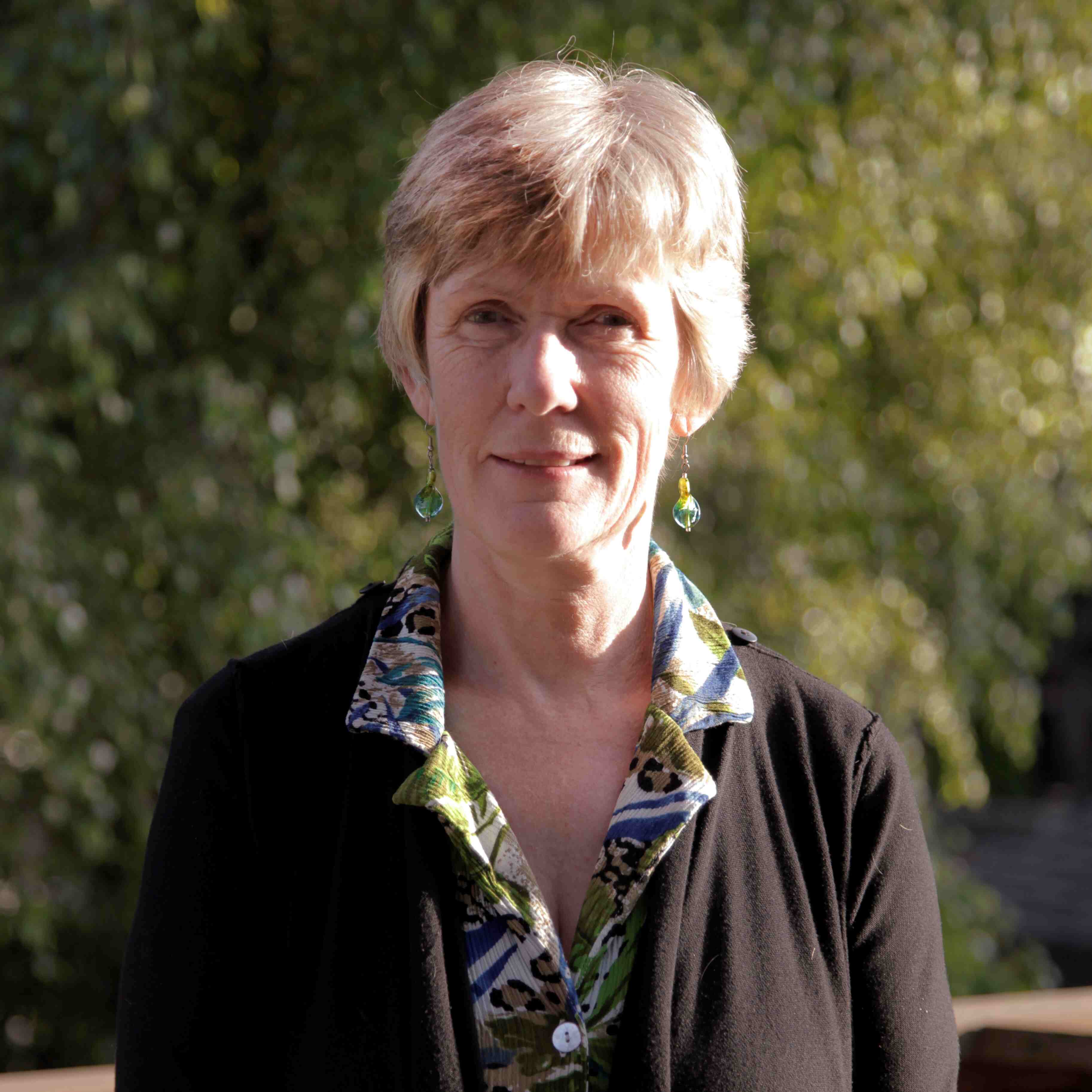 A woman wearing a black sweater with a green and blue floral blouse smiles and looks at the camera
