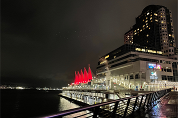 The roof arches of Canada Place in Vancouver BC are seen next to the water of Burrard Inlet, lit up in red