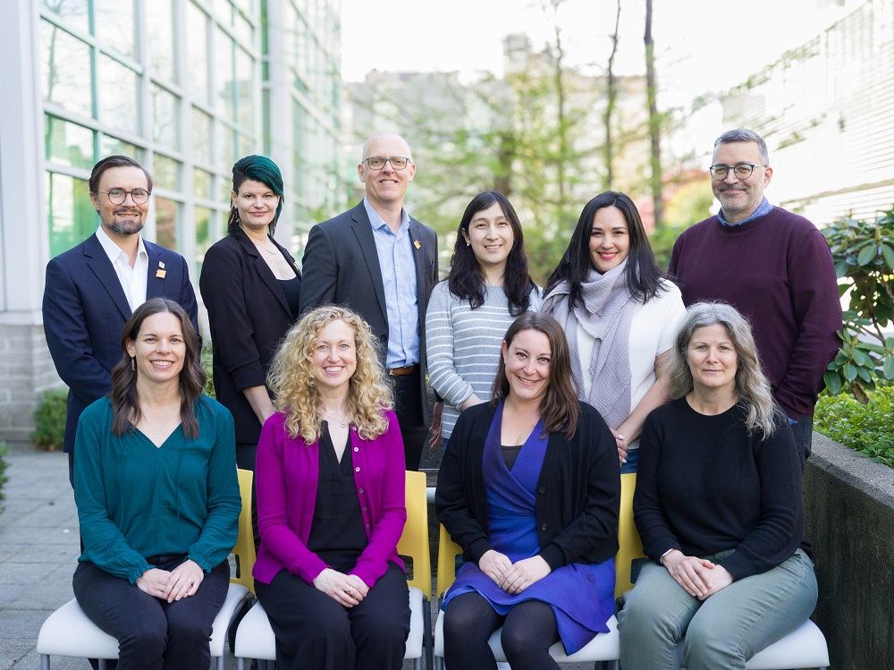 10 members of the GetCheckedOnline team pose for a photo outside the BCCDC office, four people sitting and six people standing