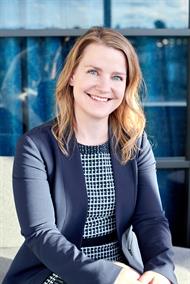 A woman with mid-length blond hair wears a navy blue blazer and smiles