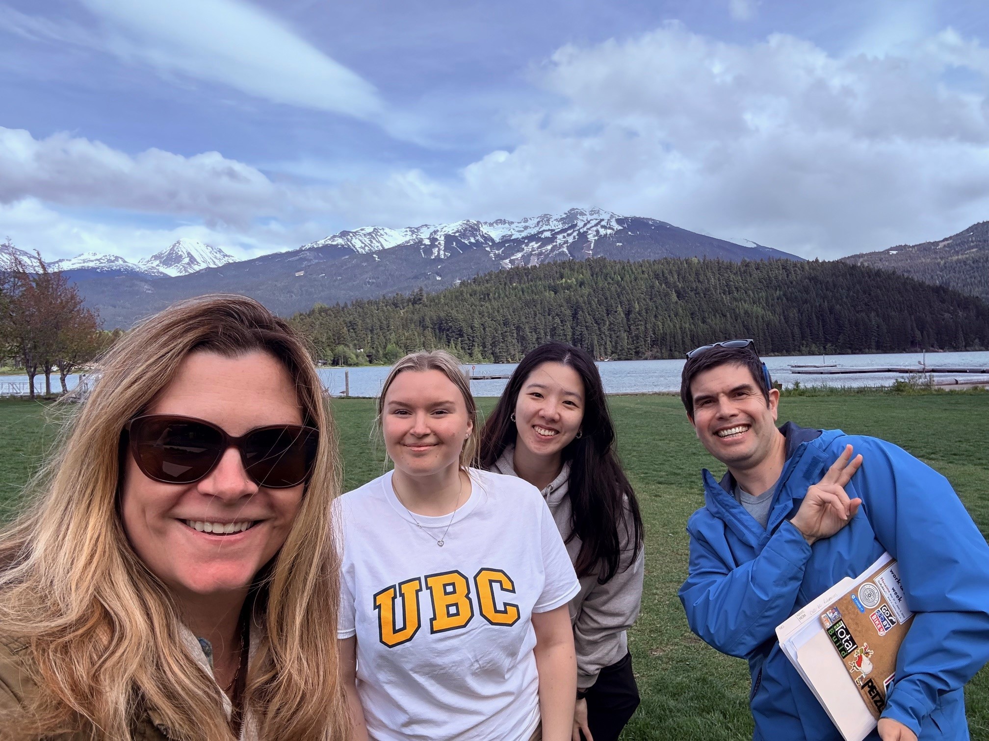 Four people stand in a grassy area with water and mountains in the background near Whistler, BC