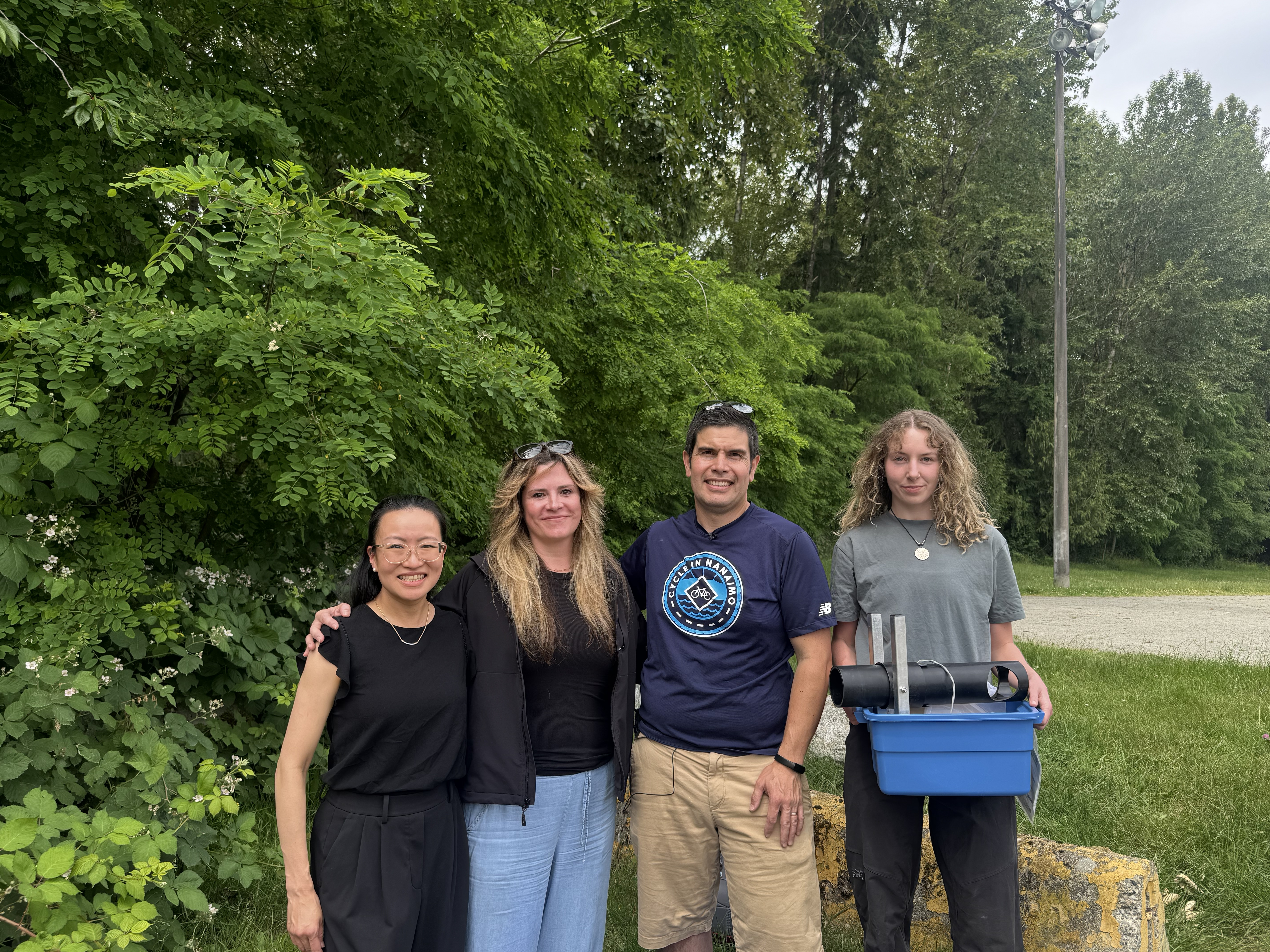 Four people stand in front of a forested area in North Vancouver, one holding a mosquito trap