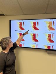 Sarah Henderson points to yellow, orange and red visual representations of smoke exposure across British Columbia from 2010-2023
